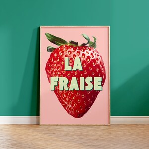 K&ouml;nnte beinhalten: Ein rosa Poster mit einer gro&szlig;en roten Erdbeere und dem Text "LA FRAISE" in gr&uuml;nen Buchstaben.