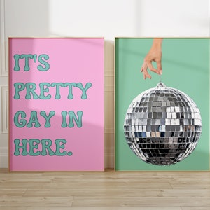 May include: Two framed prints, one with a pink background and the text "It's Pretty Gay In Here." in teal, and the other with a teal background and a silver disco ball being held by a hand.