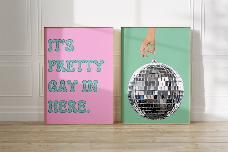 May include: Two framed prints, one with a pink background and the text "It's Pretty Gay In Here." in teal, and the other with a teal background and a silver disco ball being held by a hand.