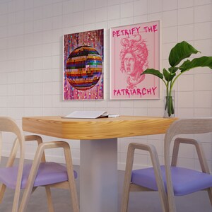 May include: Two posters on a white tiled wall, one with a disco ball and the other with a pink background and the text "Petrify the Patriarchy". A wooden table with two light purple chairs and a plant in a clear vase.