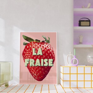 K&ouml;nnte beinhalten: Ein rosa Poster mit einer roten Erdbeere und dem Text "LA FRAISE" in gr&uuml;nen Buchstaben.
