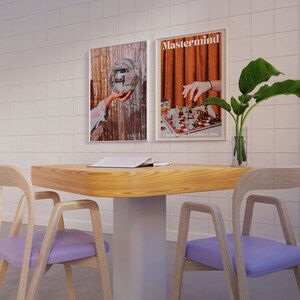 May include: Two wooden chairs with purple cushions and a wooden table with a book on top. The table has a white base. Two framed posters hang on a white tiled wall behind the table. The posters feature a disco ball and a chessboard with the text "Mastermind. Checkmate. I couldn't lose."