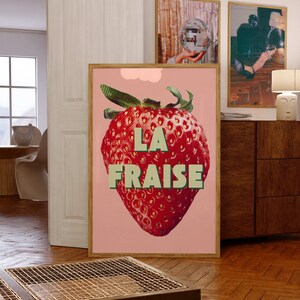 K&ouml;nnte beinhalten: Ein rosa Poster mit einer gro&szlig;en roten Erdbeere und dem Text "LA FRAISE" in gr&uuml;nen Buchstaben.