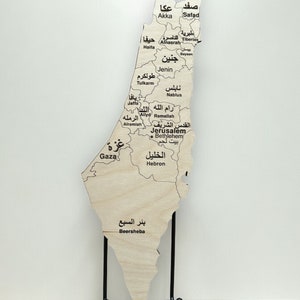 May include: A wooden map of Israel with the names of cities and towns in Arabic script. The map is mounted on a black metal stand.