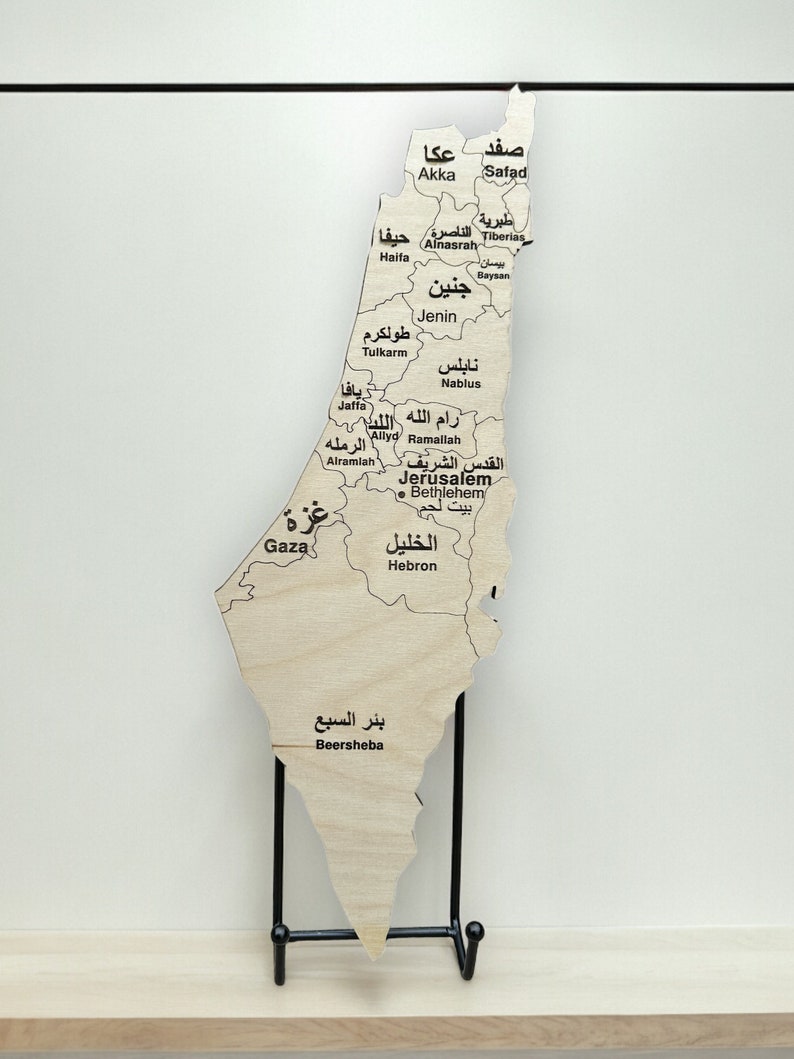 May include: A wooden map of Israel with the names of cities and towns in Arabic script. The map is mounted on a black metal stand.