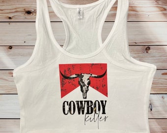 May include: White tank top with a red and white graphic of a bull skull with the text "COWBOY killer" in black.