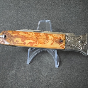 Puede incluir: Un cuchillo de bolsillo vintage con un mango de hueso con un intrincado diseño floral. El mango está decorado con un patrón tallado de flores y hojas. El cuchillo tiene una hoja de metal plateado y un mango de metal plateado.