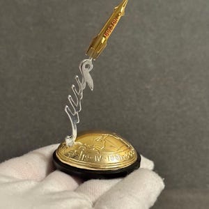 以下が含まれることがあります： 赤い文字で「VOSTOK」と書かれた、金色のロケット型の彫刻。ロケットは、黒い縁と透明な支えが付いた、金色の地球儀の台座に取り付けられています。