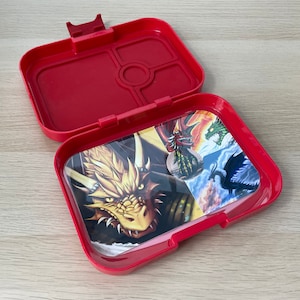 Puede incluir: Lonchera de plástico roja con una bandeja extraíble y un diseño de dragón colorido en el interior. La lonchera tiene cuatro compartimentos.