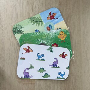 K&ouml;nnte beinhalten: Drei farbenfrohe Platzsets mit Dinosaurier- und Vogelmotiven. Die Platzsets haben ein gr&uuml;n-wei&szlig;-blaues Farbschema mit Illustrationen von Dinosauriern, V&ouml;geln und Eiern.