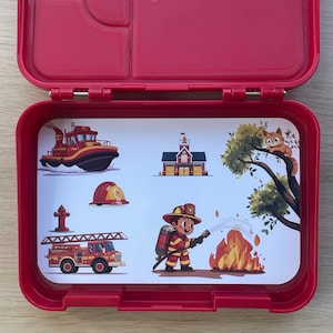 Peut inclure: Boîte à lunch rouge avec un intérieur blanc représentant un camion de pompiers, une borne d'incendie, une caserne de pompiers, un pompier, un bateau et un chat dans un arbre. La boîte à lunch a un loquet et une poignée.