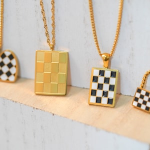 Puede incluir: Cuatro collares de oro con diferentes colgantes. Los colgantes son todos de patrones de cuadros negros y blancos. Un colgante tiene forma de corazón, uno es un cuadrado y dos son rectángulos.
