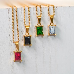 May include: Four gold necklaces with square-shaped pendants featuring different coloured gemstones. The pendants are red, black, green, and clear.