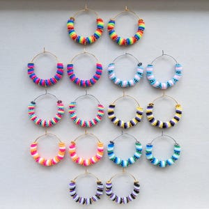 May include: A collection of hoop earrings with colorful beaded designs. The earrings feature gold-tone hoops and are adorned with beads in various color combinations, including rainbow, pink, blue, and yellow. These earrings are a fun and fashionable accessory.