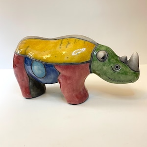 May include: A ceramic rhinoceros sculpture with a colorful patchwork design. The rhino features a yellow back, a green head, and red legs. The sculpture is a unique piece of art.