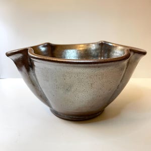 May include: A handcrafted ceramic bowl with a unique, scalloped rim. The bowl has a metallic, speckled finish in shades of gray and brown. The rim and outer edges are a darker brown, creating a contrast. This decorative bowl is ideal for serving or display.