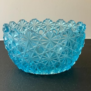 May include: A light blue glass bowl with a scalloped edge and a starburst pattern. The bowl is made of pressed glass and has a vintage look.