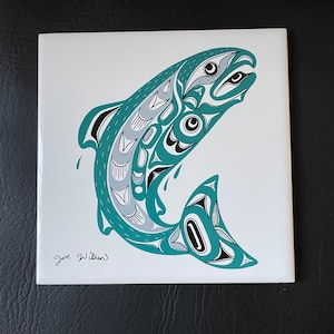 May include: A teal and gray stylized salmon design on a white ceramic tile. The tile is signed "Joe Wilson".