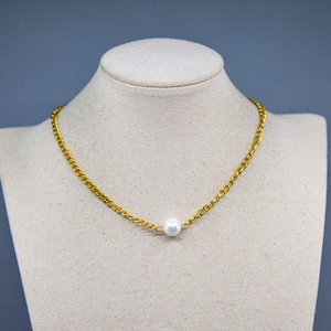 May include: A gold-colored chain necklace with a single white pearl pendant. The necklace is displayed on a mannequin with a neutral background. The chain has a curb link design.