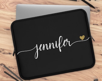May include: Black laptop sleeve with the name "Jennifer" in white script and a gold glitter heart. The sleeve has a black zipper and is on a wooden surface. Pencils and paper clips are also visible.