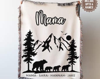 May include: A white woven throw blanket with a black mountain scene and the word "Mama" at the top. The blanket has a fringed border and the names "Mama, Sara, Hannah, Jake" are printed at the bottom.