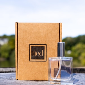 May include: A brown cardboard box with the word "tied" printed on it. A clear glass bottle with a silver cap is next to the box.