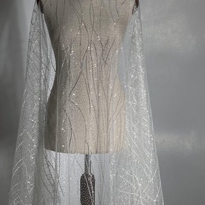 Una tela delicadamente brillante con un sutil patrón de líneas y fino brillo. Perfecta para vestidos de noche, vestidos de novia y velos de novia.