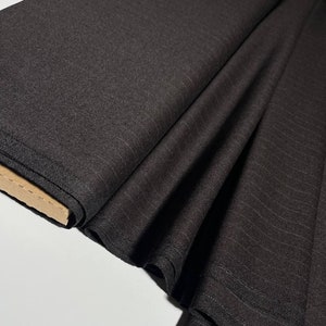 Op de afbeelding: Zwarte stof met een subtiel streepjespatroon. De stof is gevouwen en opgerold, waardoor de textuur en de weving zichtbaar zijn.