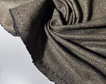 May include: Close-up of a folded fabric with a herringbone pattern. The fabric is a mix of brown and black threads, creating a textured appearance. The edges of the fabric are visible, showing the raw, unfinished cut.