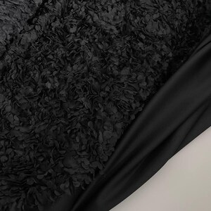 Peut inclure: Tissu noir avec une surface texturée et plissée. Le tissu est doux et présente un motif délicat ressemblant à des fleurs.