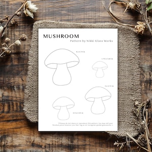 May include: A white paper featuring mushroom patterns and the text "MUSHROOM Pattern by Nikki Glass Works." The patterns include mushroom outlines with measurements: 10.16 x 9.53 cm, 4.45 x 4.19 cm, 7.62 x 6.99 cm, and 6.35 x 5.72 cm. The paper is on a burlap cloth.