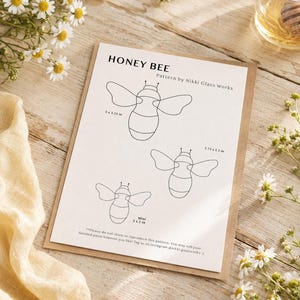 Puede incluir: Un patrón de papel blanco titulado HONEY BEE de Nikki Glass Works que presenta tres ilustraciones de abejas en líneas negras con dimensiones etiquetadas como 5 x 3.25 pulgadas, 3.75 x 2.5 pulgadas y una versión mini de 3 x 2 pulgadas.