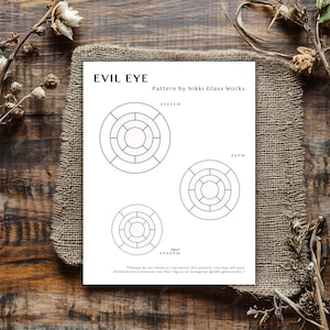 Könnte beinhalten: Ein weißes Musterblatt mit dem Text "EVIL EYE" und drei kreisförmigen Designs. Die Designs sind mit den Größen 8,9 x 8,9 cm, 7,6 x 7,6 cm und 6,4 x 6,4 cm beschriftet. Das Blatt liegt auf einem Jutegewebe über einer Holzoberfläche.