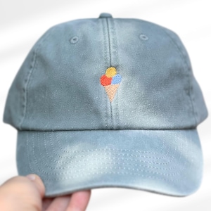 Peut inclure: Casquette de baseball bleu poussiéreux avec une visière incurvée. La casquette présente un motif de cornet de glace brodé avec des boules de glace rouges, jaunes et bleues. Fabriqué en tissu doux et durable.