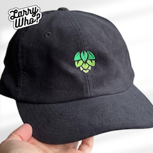 Könnte beinhalten: Schwarze Baseballkappe mit einem grünen und gelben Hopfen-Design. Die Kappe hat einen gebogenen Schirm und einen Stoffriemenverschluss. Der Text "Larry Who?" befindet sich oben links auf der Kappe.