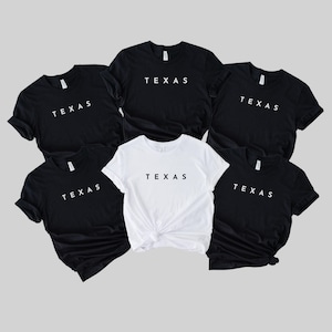 May include: Six t-shirts with the word "TEXAS" printed in white on a black background. One t-shirt is white with black text.