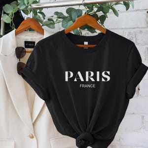 May include: Black short-sleeved t-shirt with white text that reads "PARIS FRANCE".