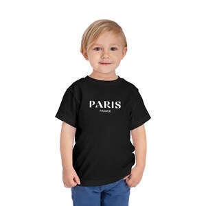 May include: A black t-shirt with white text that says "PARIS FRANCE" on it. A young child is wearing the shirt.