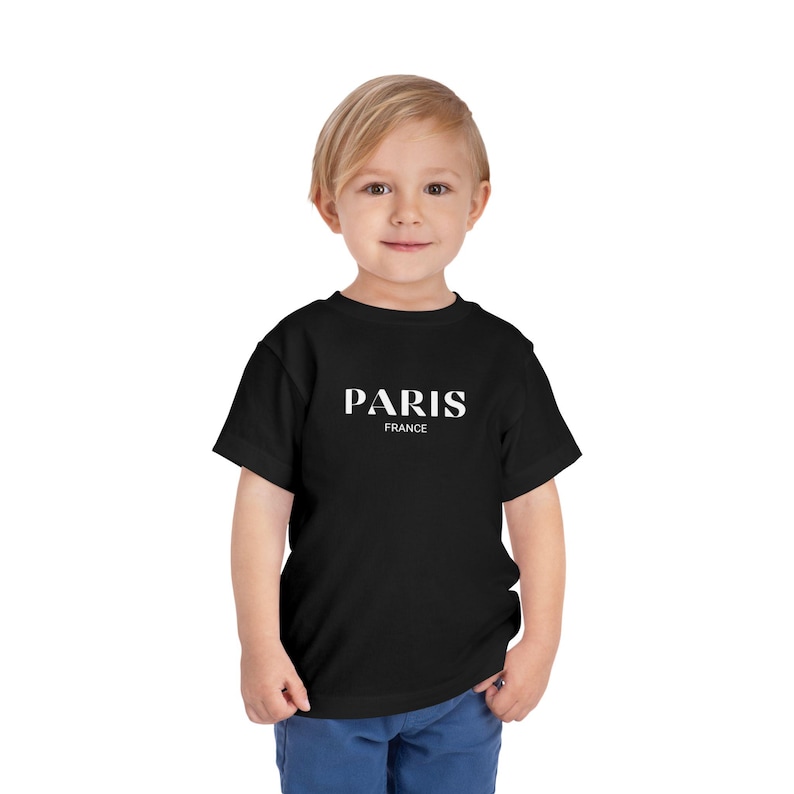 May include: A black t-shirt with white text that says "PARIS FRANCE" on it. A young child is wearing the shirt.