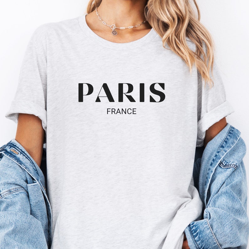 May include: A grey t-shirt with the word "PARIS" in black letters and the word "FRANCE" underneath in smaller black letters.