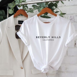 May include: White t-shirt with black text that reads "Beverly Hills California".