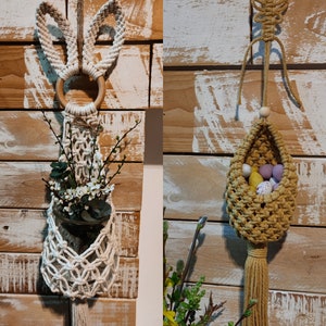 May include: Two macrame wall hangings. The first is a white macrame planter with bunny ears and a wooden ring, holding greenery and white flowers. The second is a tan macrame basket with a tassel, holding decorative eggs. Both are suspended from wooden rings.