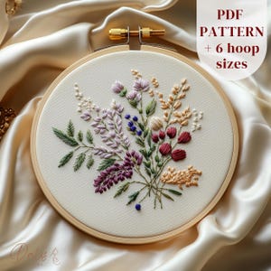 May include: Embroidered floral hoop art featuring a variety of flowers in shades of purple, pink, red, and green. The hoop is made of wood and has a white fabric background. The text "PDF PATTERN + 6 hoop sizes" is printed in black at the top of the image.