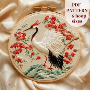 May include: Embroidered crane design in a wooden hoop. The crane has white feathers, a black neck, and red accents. Red flowers and green foliage surround the crane. The text "PDF PATTERN + 6 hoop sizes" is visible.