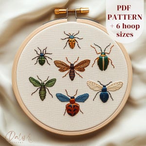 May include: Embroidered insect designs in a wooden embroidery hoop. The insects include a bee, a ladybug, a green beetle, and a blue beetle. The text "PDF PATTERN + 6 hoop sizes" is visible in the top right corner.