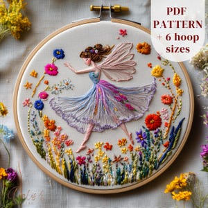 May include: An embroidered artwork in a wooden hoop, depicting a fairy in a flowing dress amidst vibrant flowers. The fairy has detailed wings, set against a white backdrop. The text "PDF PATTERN + 6 hoop sizes" is displayed.