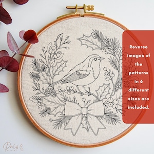 May include: A circular wooden embroidery hoop containing a cream-colored fabric with a black line art design of a bird perched within a wreath of holly leaves, berries, and pine needles, featuring a bow at the bottom and text about reverse patterns.