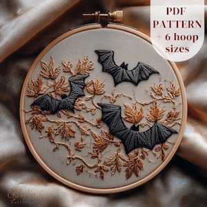 Puede incluir: Arte de aro bordado con tres murciélagos negros y hojas de otoño en tonos dorados y marrones. El diseño está sobre un fondo de tela neutra, enmarcado por un aro de madera. El texto en la imagen dice "PDF PATTERN + 6 hoop sizes."