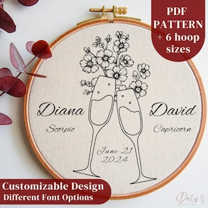 Op de afbeelding: Een borduurring met een bloemenontwerp en twee champagneglazen, met de namen "Diana" en "David" en de datum "21 juni 2024". De tekst "PDF Pattern + 6 hoop sizes" en "Customizable Design Different Font Options" zijn ook zichtbaar.
