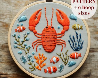 May include: Embroidered hoop art featuring an orange lobster and colorful fish, coral, and seaweed on a light gray background. The text "PDF PATTERN + 6 hoop sizes" is in the upper right corner. The embroidery is set in a wooden hoop.